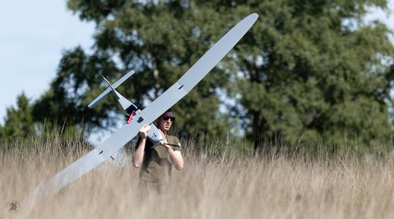 Een man loopt met een drone door het hoge gras