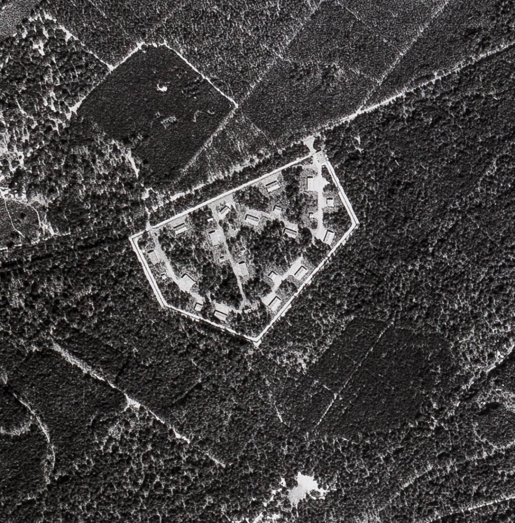 Zwart-wit luchtfoto met veel bos en in het midden het complex