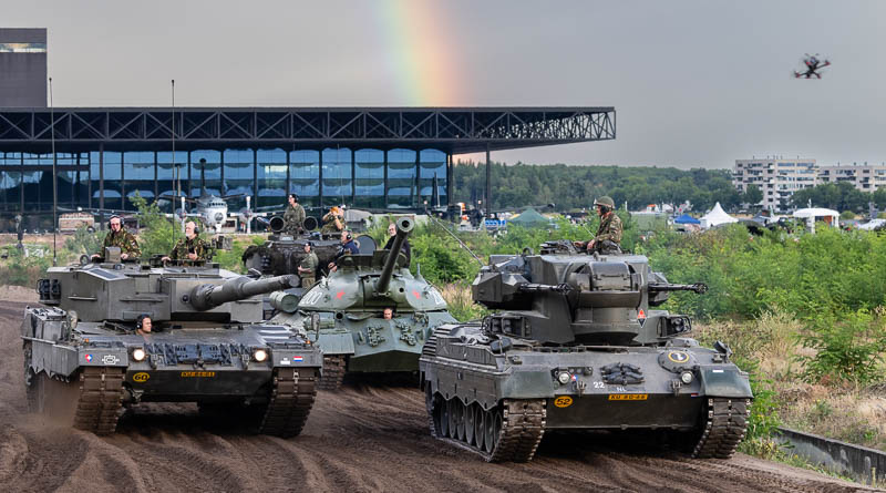 Drie tanks met op de achtergrond een donkere lucht met regenboog
