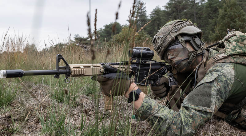 Militair met geweer in de aanslag, liggend in het gras
