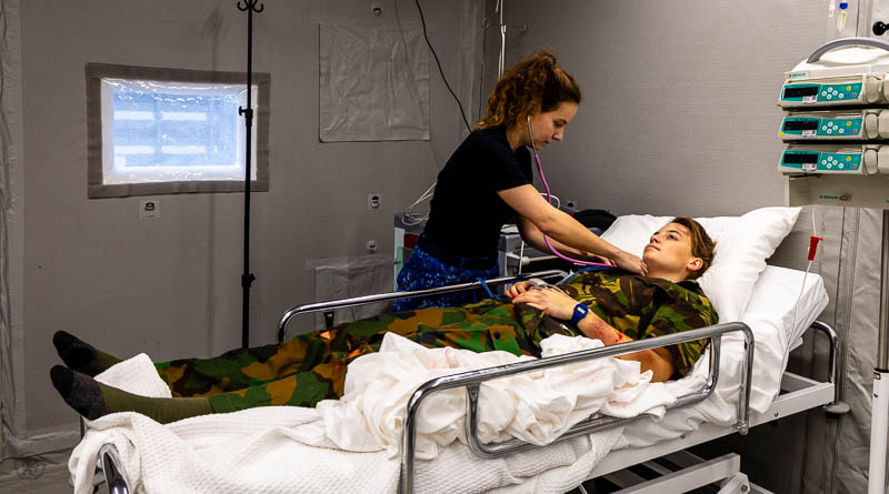 Militaire arts onderzoekt militair in ziekenhuisbed