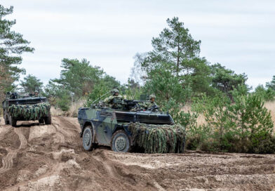 Twee militaire voertuigen (Fenneks) rijden door diepe sporen in het zand