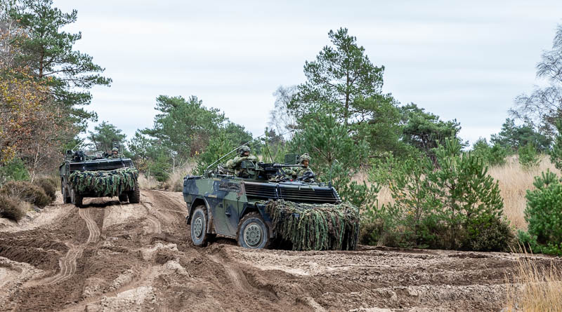Twee militaire voertuigen (Fenneks) rijden door diepe sporen in het zand