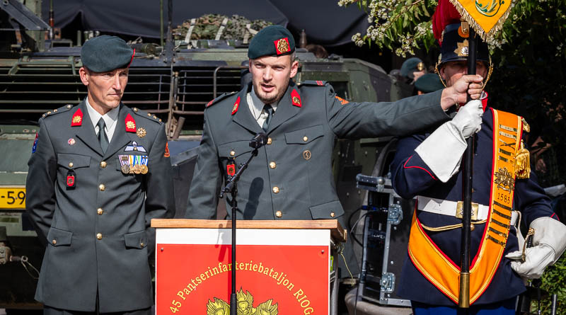 Een militair houdt het vaandel vast en zegt de eed op. Zijn commandant kijkt toe.