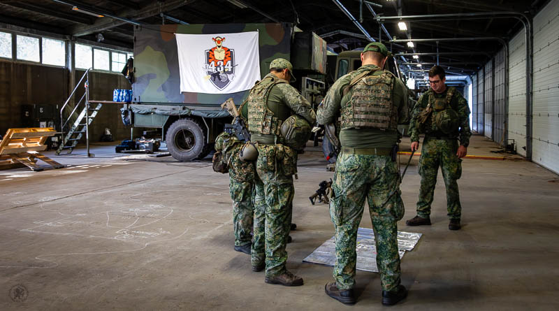 Militairen rond een kaart met op de achtergrond het logo van 434 Herstel